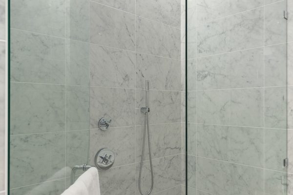 Luxury penthouse bathroom with marble walls and floors, freestanding bathtub, frameless glass shower, and floral light fixture