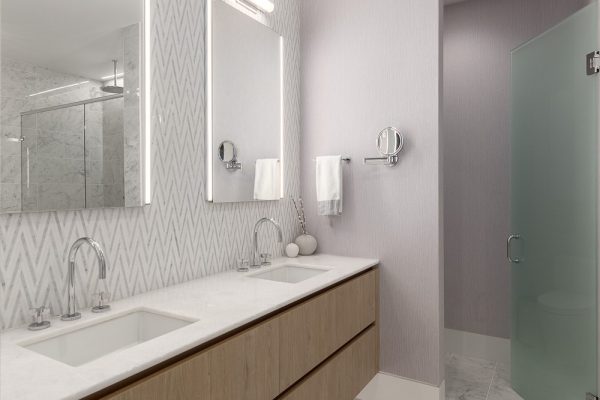 Modern penthouse bathroom with chevron wallpaper, double vanity, marble countertops, and frosted glass shower