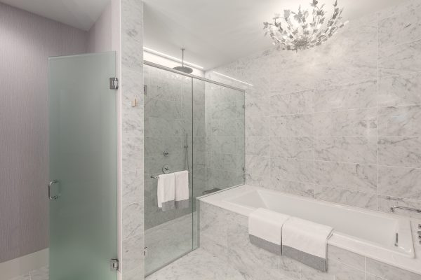Luxury penthouse bathroom with marble walls and floors, freestanding bathtub, frameless glass shower, and floral light fixture