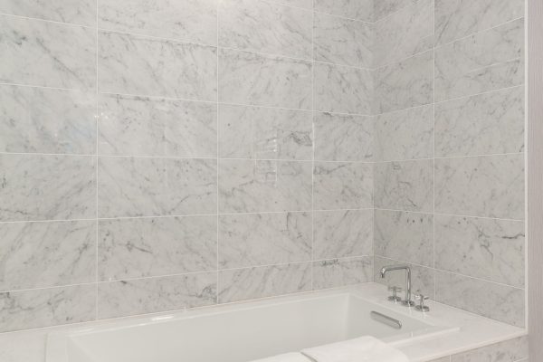 Luxury penthouse bathroom with marble walls and floors, freestanding bathtub, frameless glass shower, and floral light fixture
