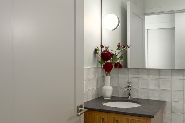 Powder room vanity with floral arrangement, tile backsplash, and circular light fixture